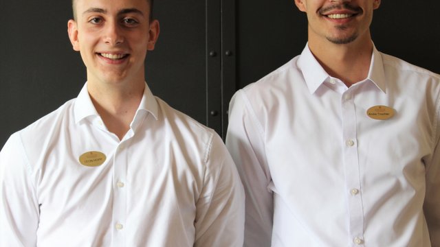 Romantik Hotel Hirschen: Blog Zwei junge Männer in weißen Hemden und Namensschildern vor dunklem Hintergrund