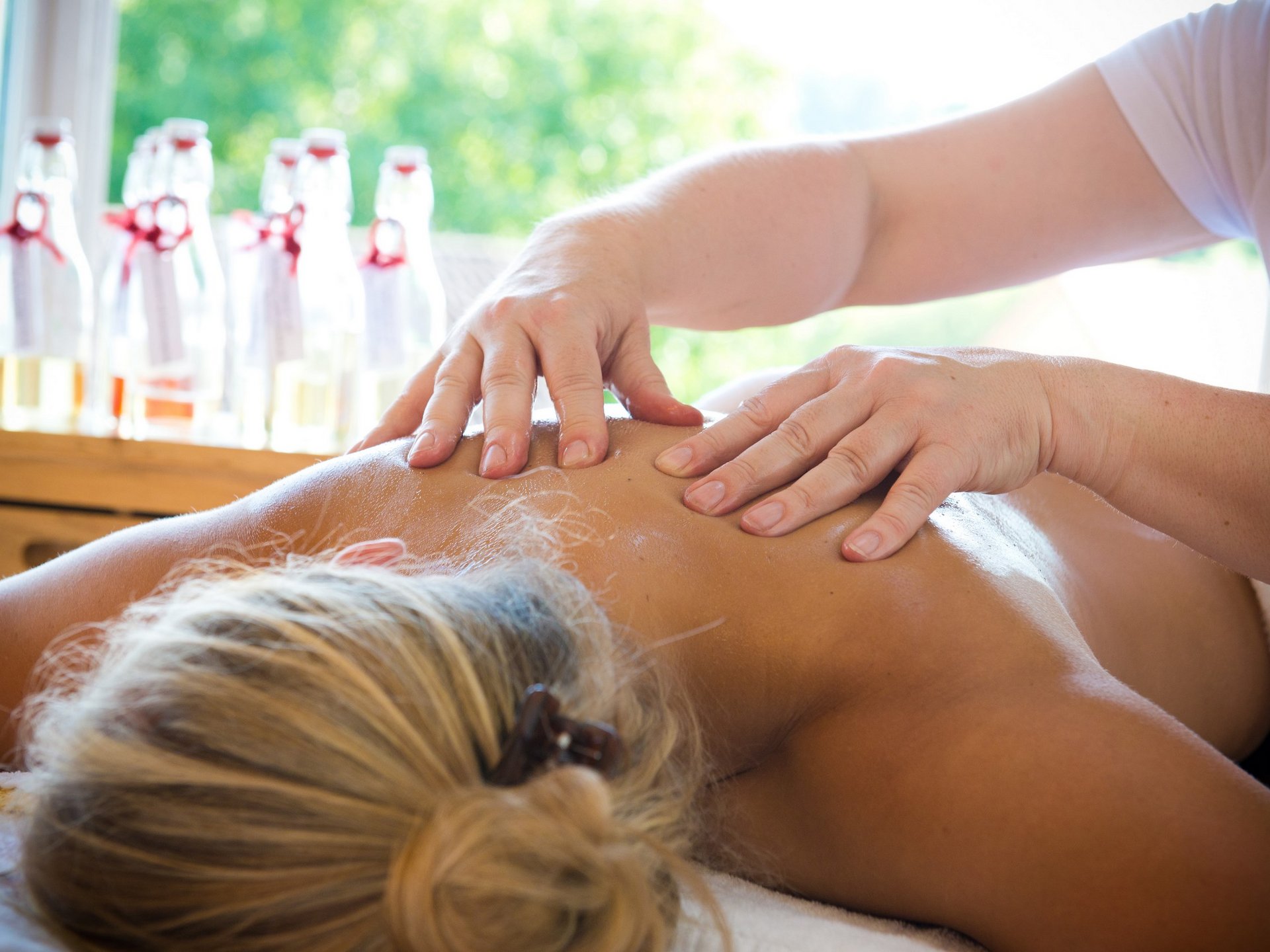 Wellness Person receiving a back massage in a bright room with glass bottles in the background