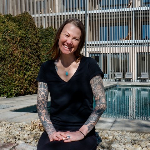 Tageswellness in der Oberpfalz Frau mit Tattoos sitzt lächelnd vor Pool und modernem Gebäude