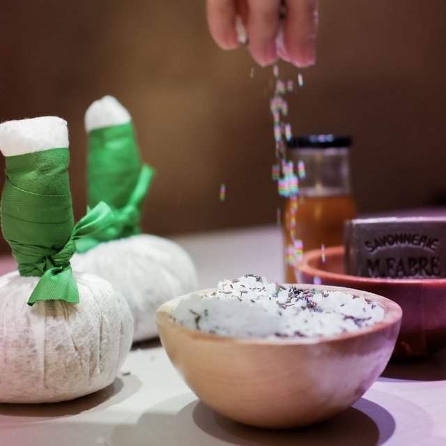Alles Wichtige für Deinen Aufenthalt im Hirschen Hand streut Salz in Schale mit Kräutern, Spa-Accessoires im Hintergrund