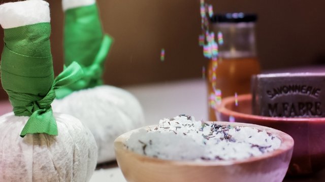 Golfurlaub Bayern: Platzhirsch oder Anfänger? Hand streut Salz in Schale mit Kräutern, Spa-Accessoires im Hintergrund