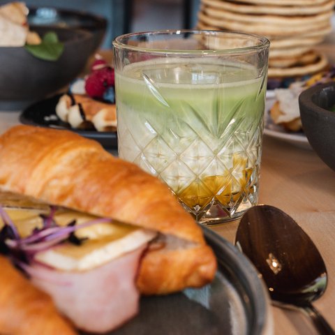Brunch - das Langschläferfrühstück Croissant mit Schinken und Käse neben einem Glas mit zwei Schichten Getränk
