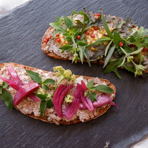 Romantik Hotel Hirschen: Frühstück Zwei Scheiben Brot mit Aufstrich, roten Zwiebeln, Kräutern und Pfefferkörnern auf Schieferplatte