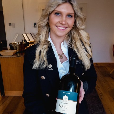 Restaurant in Parsberg: Gourmet genießen Frau hält eine Flasche Saffredi Rotwein 2016 und lächelt in Innenraum