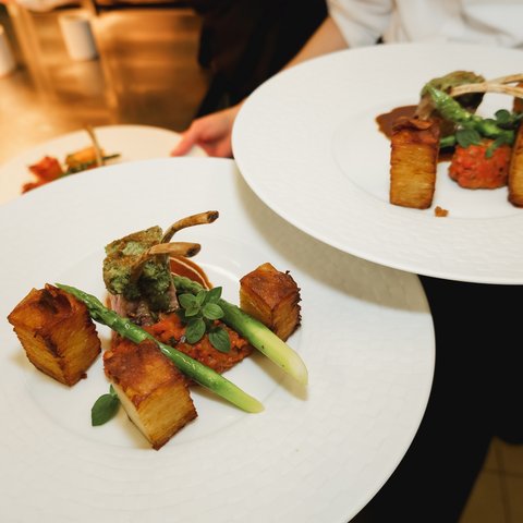 Restaurant in Parsberg: Gourmet genießen Fein angerichtete Lammkoteletts mit Kartoffeln, Spargel und Tomatensauce auf weißen Tellern.