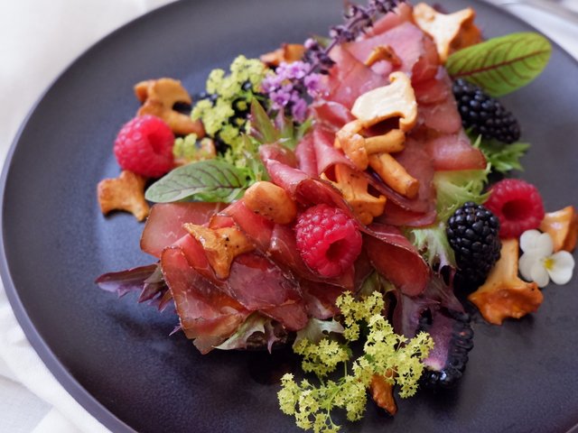 Romantik Hotel Hirschen: Bildergalerie Salat mit getrocknetem Fleisch, Pfifferlingen, Himbeeren und Brombeeren auf schwarzem Teller
