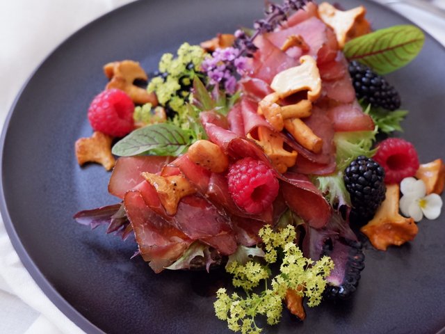 Romantik Hotel Hirschen: Bildergalerie Salat mit getrocknetem Fleisch, Pfifferlingen, Himbeeren und Brombeeren auf schwarzem Teller