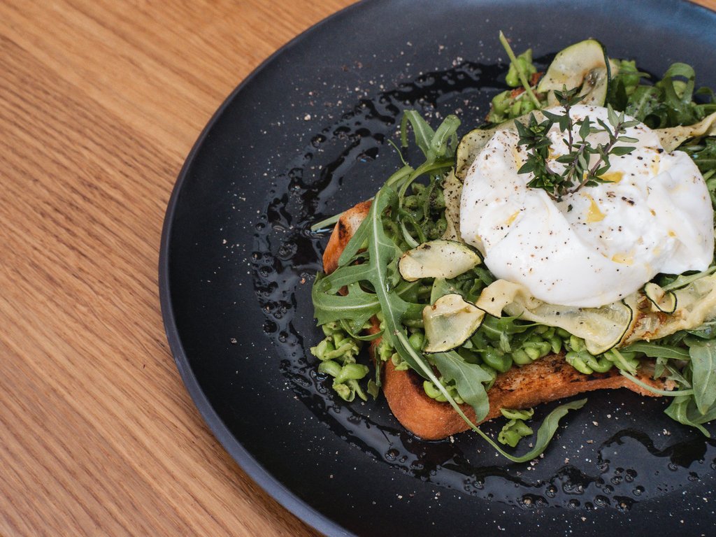 Workation Toast mit Avocado, Rucola, Zucchinichips und pochiertem Ei auf schwarzem Teller