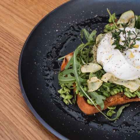 Guesthouse in Parsberg: A salute to great taste Toast with avocado, arugula, zucchini chips, and poached egg on black plate