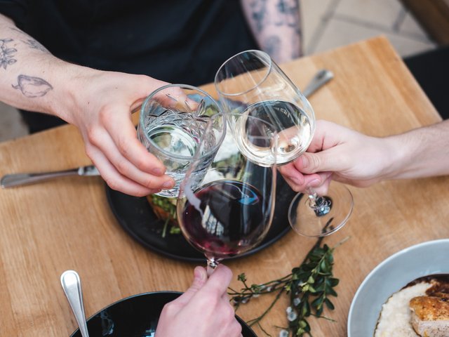 Romantik Hotel Hirschen: Bildergalerie Drei Personen stoßen mit Rotwein, Weißwein und Wasser über einem Esstisch an