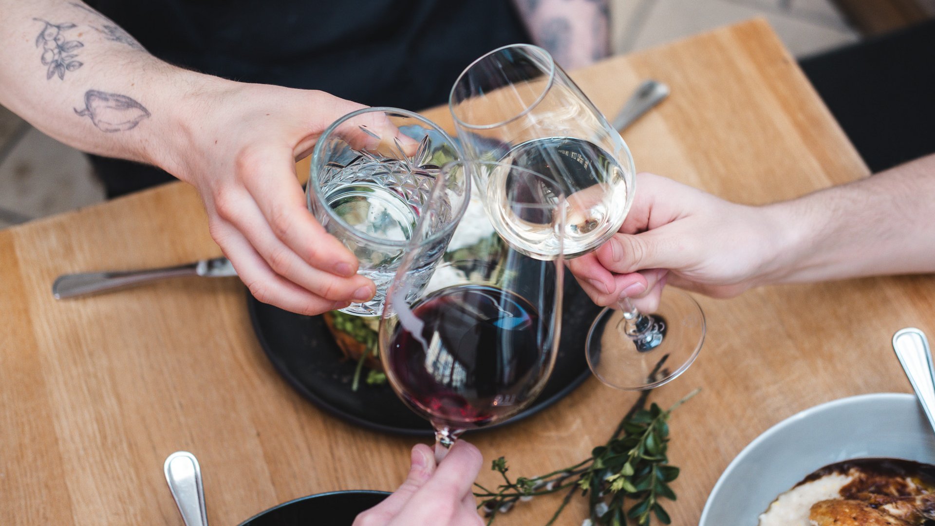 Romantik Hotel Hirschen: Kulinarik Drei Personen stoßen mit Rotwein, Weißwein und Wasser über einem Esstisch an