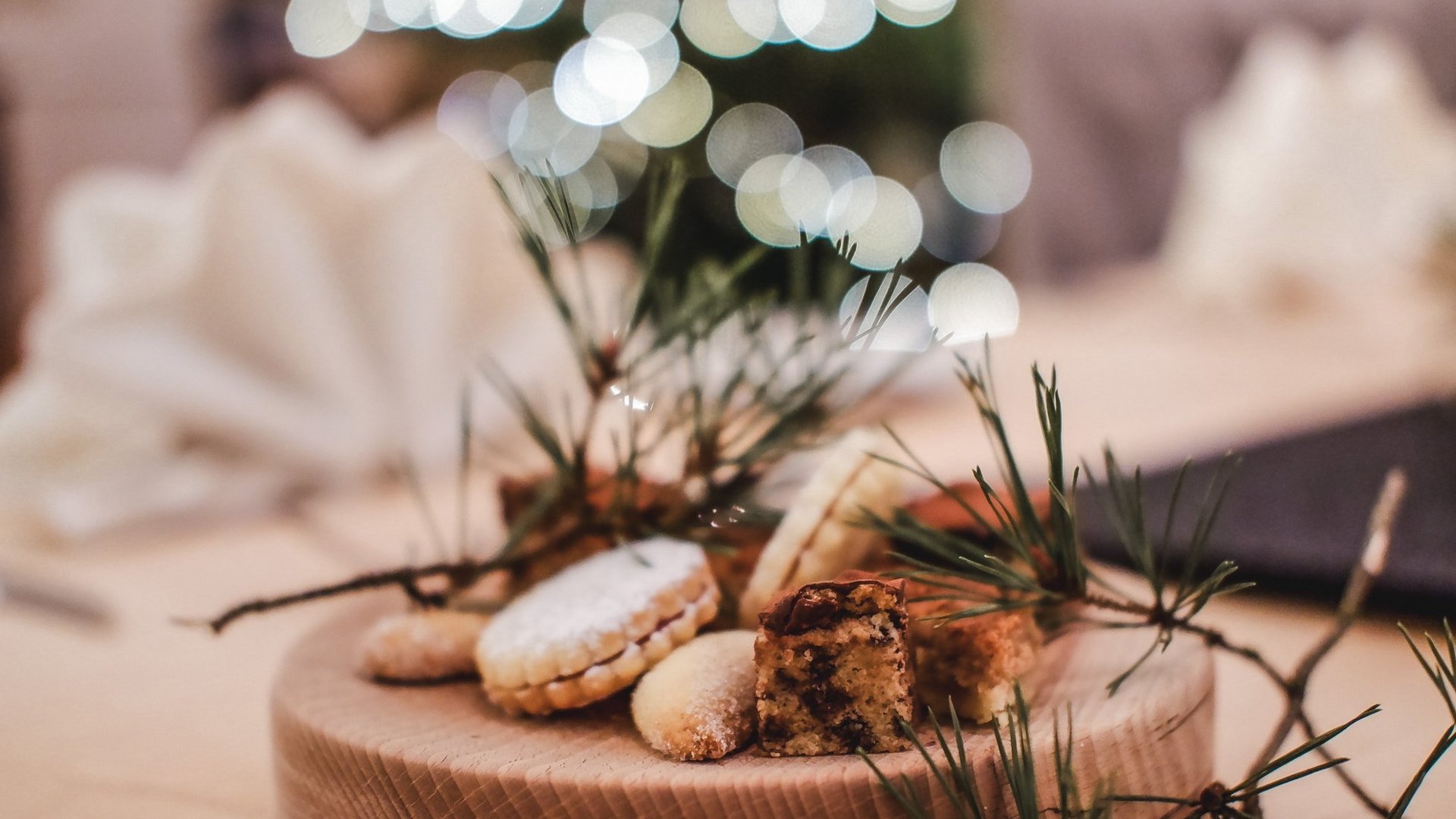 Gasthof Parsberg: Ein Gruß an den guten Geschmack Weihnachtsplätzchen mit Tannenzweigen auf Holzplatte, unscharfer Hintergrund mit Lichtern