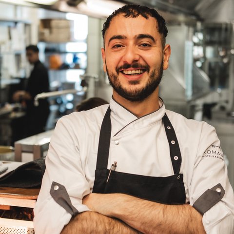 Gasthof Parsberg: Ein Gruß an den guten Geschmack Lächelnder Koch mit weißer Uniform und schwarzer Schürze in professioneller Küche