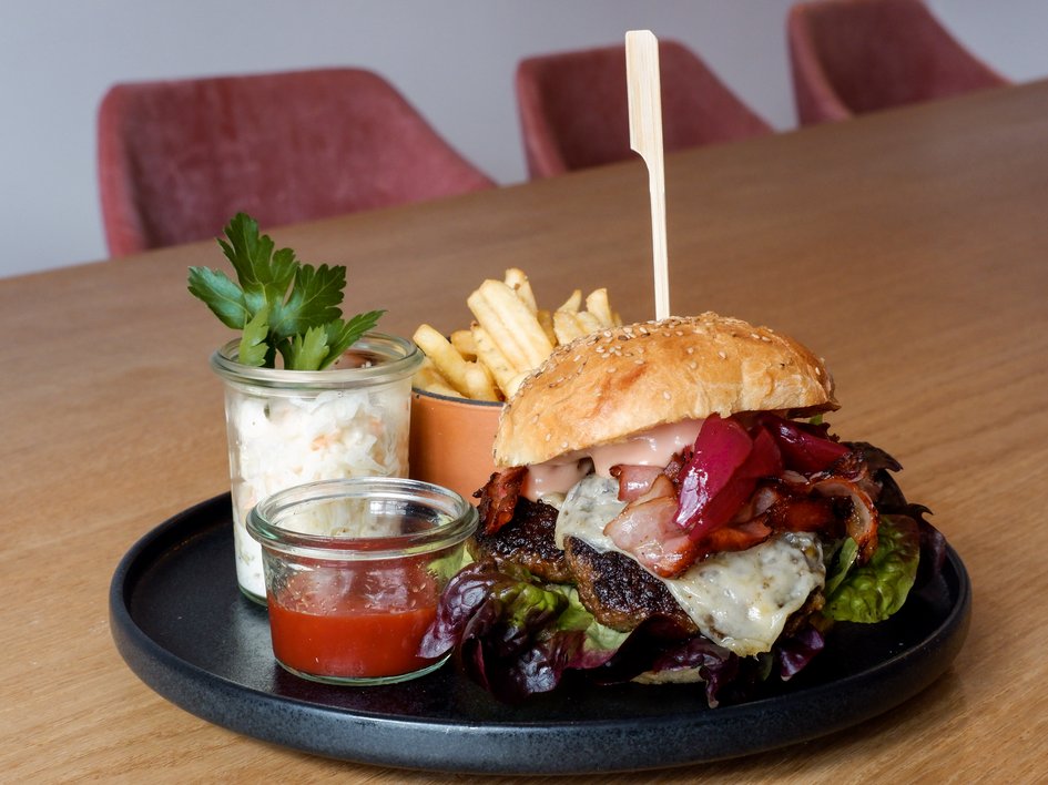 Gasthof Parsberg: Ein Gruß an den guten Geschmack Burger mit Speck, Käse, Pommes, Krautsalat und Ketchup auf schwarzem Teller