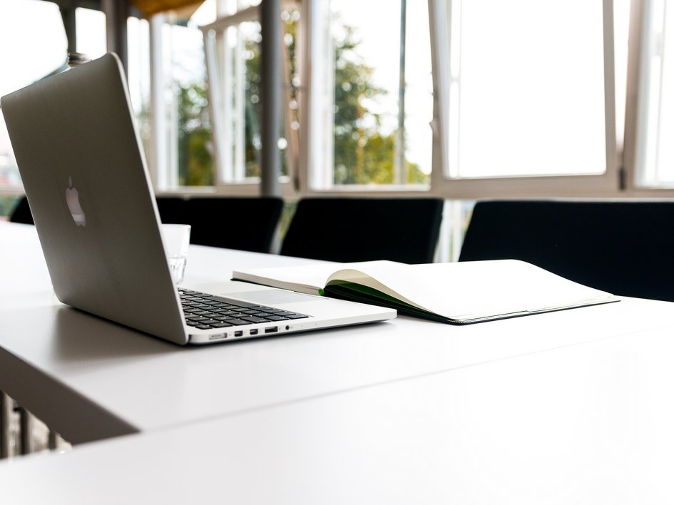 Tagung mit Mehrwert Offener Laptop und Buch auf einem weißen Tisch in einem Besprechungsraum