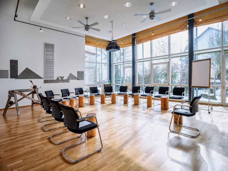 Looking for somewhere for conferences in Bavaria? Meeting room with chairs and wooden stools arranged in a circle by large windows