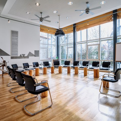 Looking for somewhere for conferences in Bavaria? Meeting room with chairs and wooden stools arranged in a circle by large windows