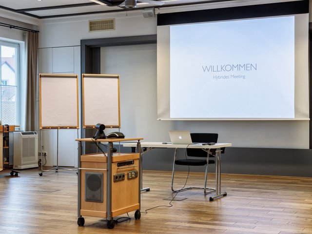 Romantik Hotel Hirschen: Bildergalerie Leerer Konferenzraum mit Leinwand, Flipcharts und Laptop für hybrides Meeting