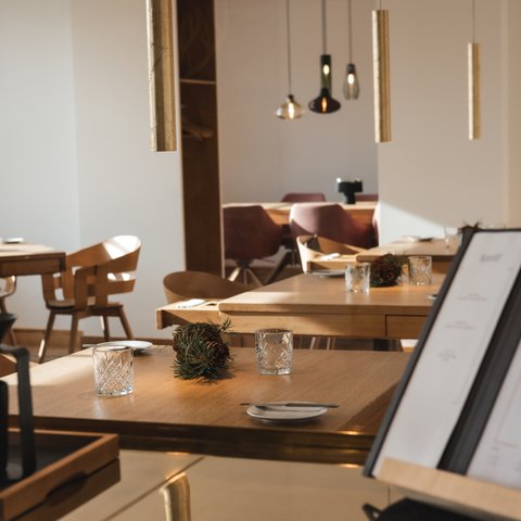 Romantik Hotel Hirschen: Gastgeber & Werte Modernes Restaurant mit Holz Tischen, Gläsern und Menü auf Halterung