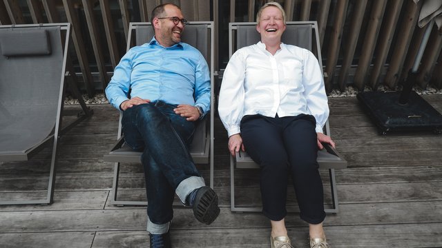 Hotel Oberpfalz: Urlaubsluft schnuppern! Zwei lachende Personen sitzen auf Liegestühlen auf Holzterrasse