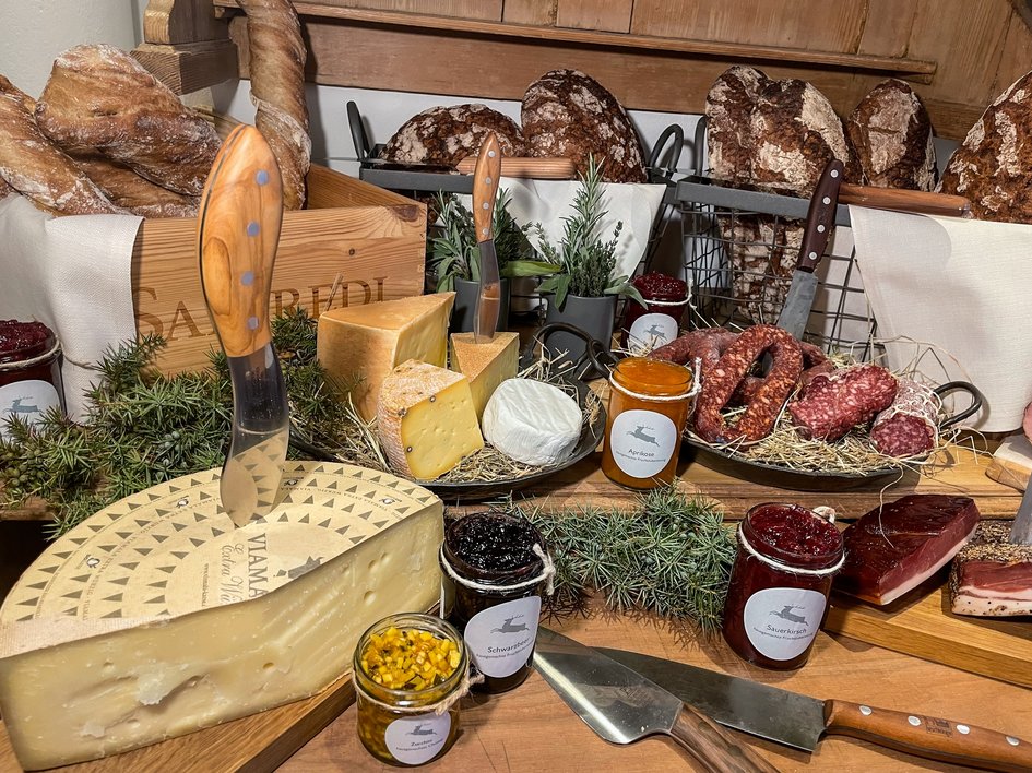 Nachhaltige Hotels in Deutschland gesucht? Verschiedene Käsesorten, Brot, Wurst und Marmeladen auf einem Holztisch arrangiert