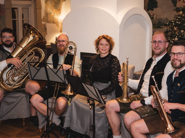 Romantik Hotel Hirschen: Bildergalerie Fünf Musiker in traditioneller Tracht mit Blechblasinstrumenten vor Kamin und Weihnachtsbaum