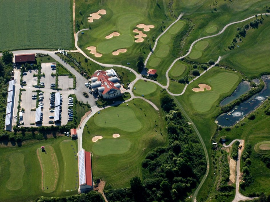 Golf holiday in Bavaria: top boss or beginner? Aerial view of a golf course with buildings, parking lots, and water features