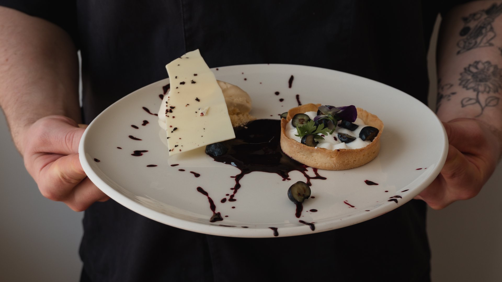 Restaurant in Parsberg: Gourmet genießen Hand hält Teller mit Desserttarte, Beeren, weißer Schokolade und Soße