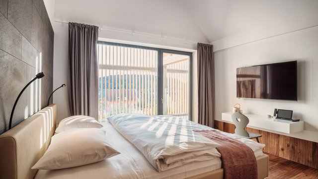 Wellnesshotel in der Oberpfalz: schwitzen & schwimmen Modernes Schlafzimmer mit großem Bett, Fensterfront und Wandfernseher
