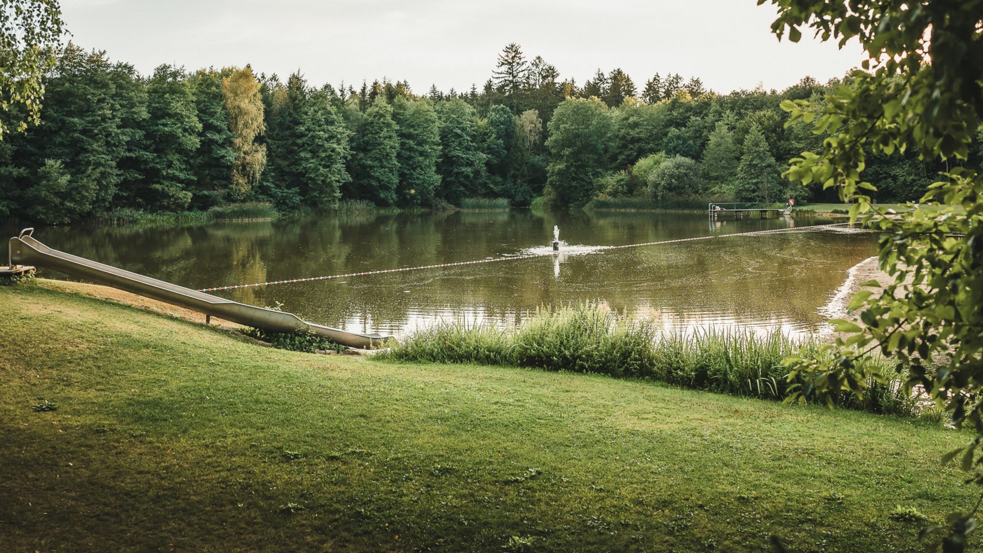 Badeseen Grüner Park mit Teich, Wasserrutsche und Bäumen im Hintergrund