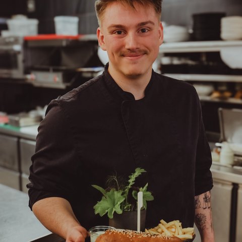 Gasthof Parsberg: Ein Gruß an den guten Geschmack Koch hält Teller mit Sandwich, Pommes und Kräutern in einer Restaurantküche