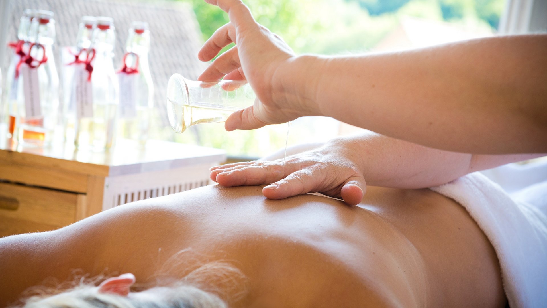 Wellness Massage oil being poured on the back of a person lying in a spa