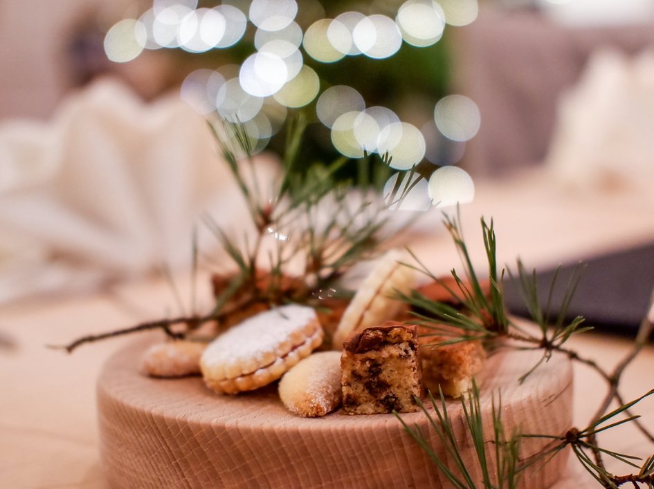 Weihnachtsmenüs 2025 Weihnachtsplätzchen auf Holzbrett mit Tannenzweigen und Lichterketten im Hintergrund