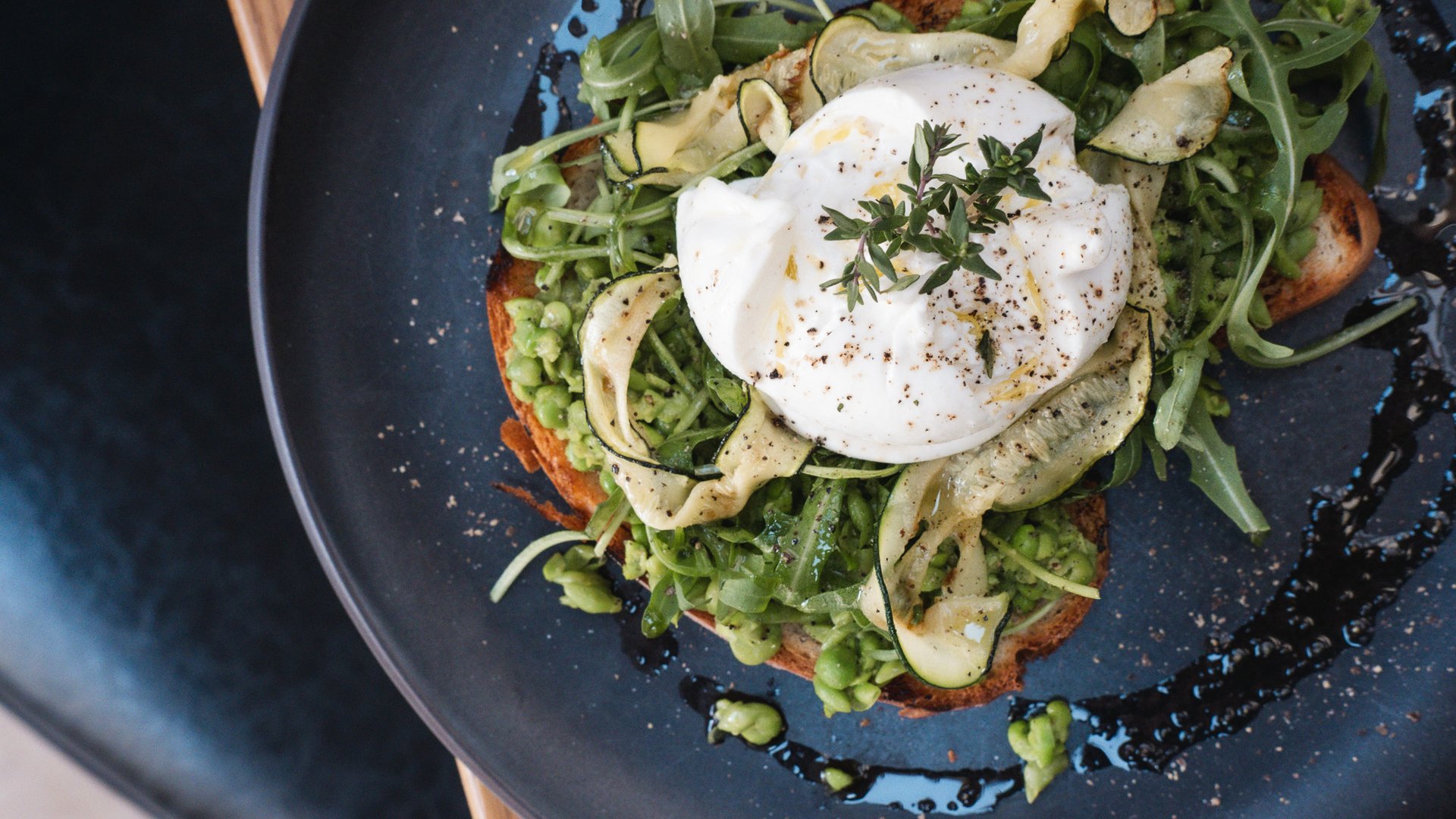 Romantik Hotel Hirschen: Kulinarik Toast mit Avocado, Rucola, Zucchini und pochiertem Ei auf schwarzem Teller