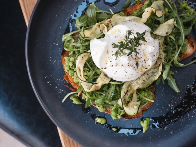 Romantik Hotel Hirschen: Bildergalerie Toast mit Avocado, Rucola, Zucchini und pochiertem Ei auf schwarzem Teller
