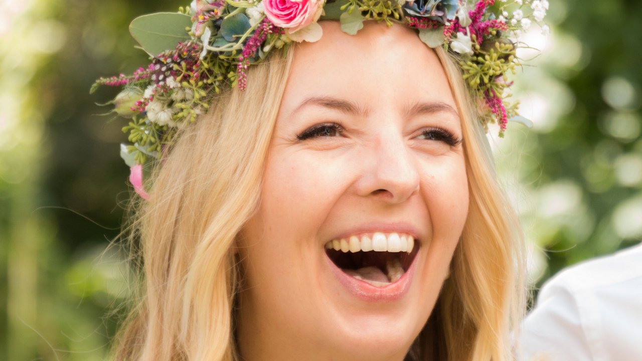 Heiraten bei uns Lachende Frau mit Blumenkopfschmuck bei sonnigem Outdoor-Event