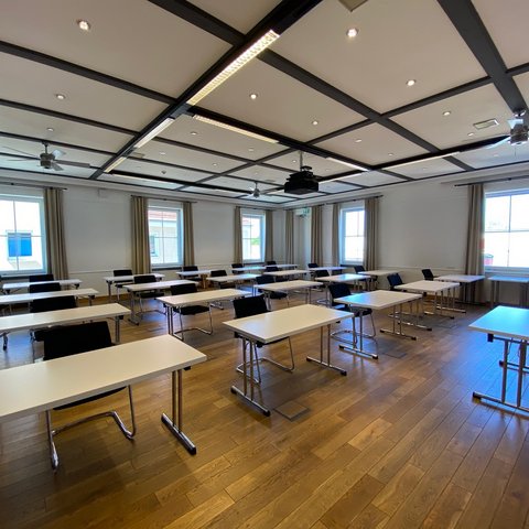 Looking for somewhere for conferences in Bavaria? Empty classroom with white desks, black chairs, and wooden floor