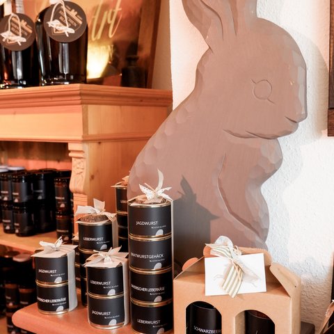 Nachhaltiges Hotel in Bayern mit Hirschenmanufaktur Holzhasenfigur neben Dosen mit bayerischen Wurst- und Käseprodukten