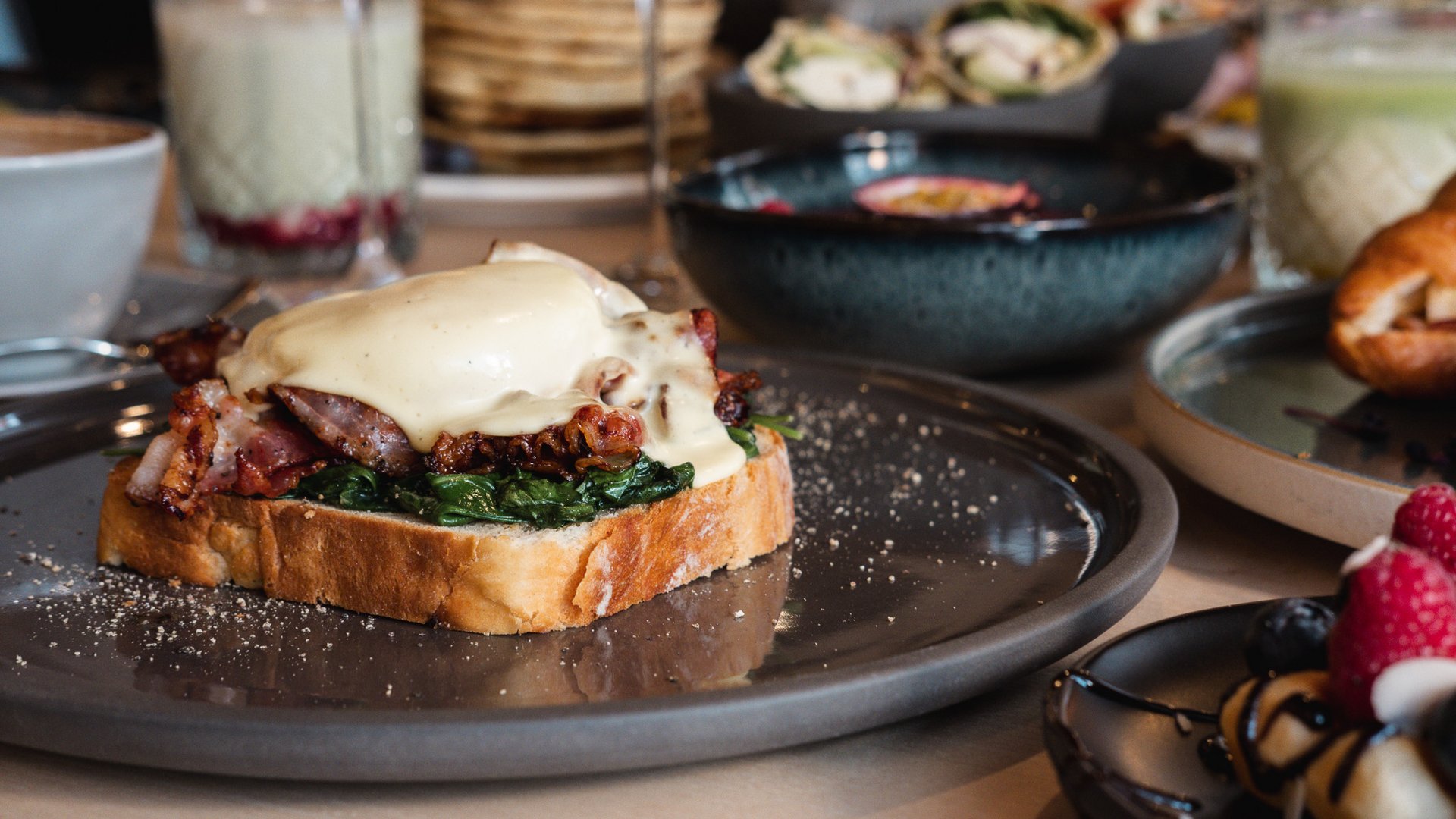 Brunch – breakfast for late risers Toast with spinach, bacon, and hollandaise sauce on a gray plate