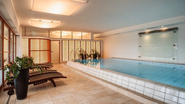Romantik Hotel Hirschen: Blog Innenpool mit Liegestühlen und Pflanzen in modernem Wellnessbereich