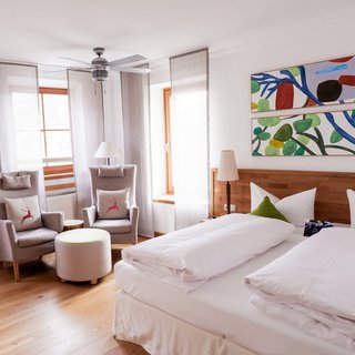 Hochzeitslocation Oberpfalz gesucht? Helles Hotelzimmer mit Doppelbett, zwei Sesseln und abstrakter Kunst an der Wand