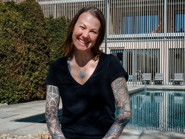 Romantik Hotel Hirschen: Bildergalerie Frau mit Tätowierungen sitzt lächelnd vor modernem Gebäude und Pool