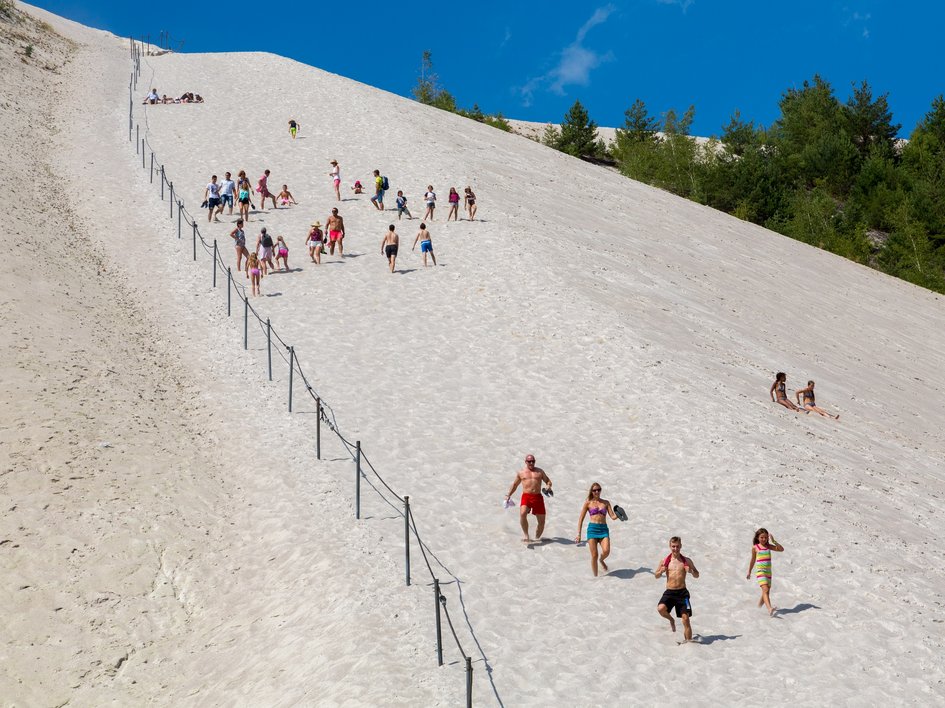 Wandern in der Oberpfalz: Aktiv in der Natur Menschen klettern und spielen auf einem großen Sandhügel unter blauem Himmel