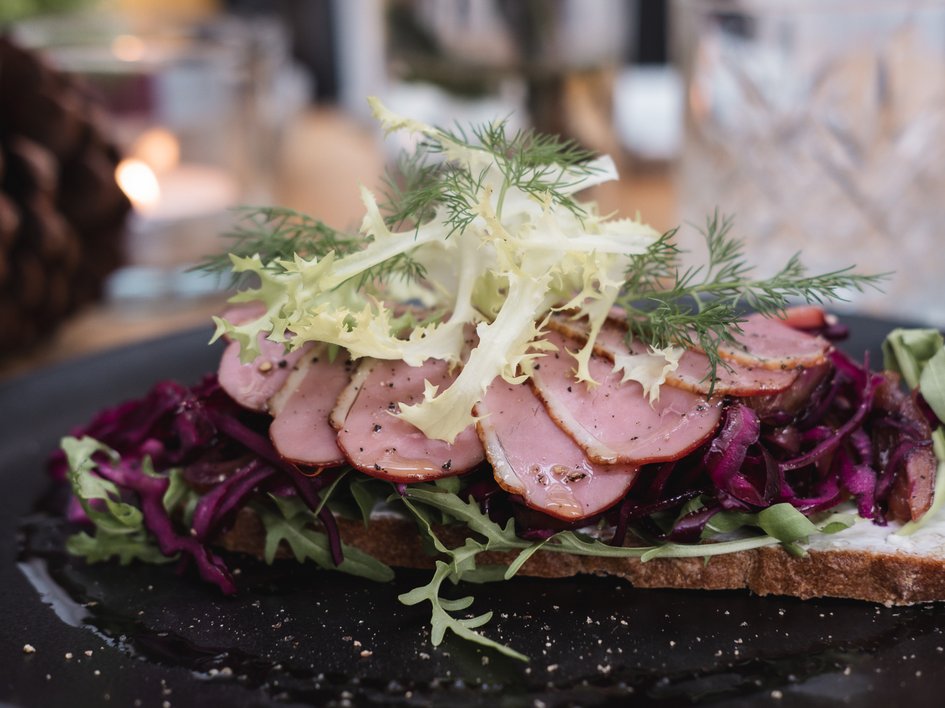Gasthof Parsberg: Ein Gruß an den guten Geschmack Offenes Sandwich mit Räucherente, Salat und Rotkohl auf dunklem Teller