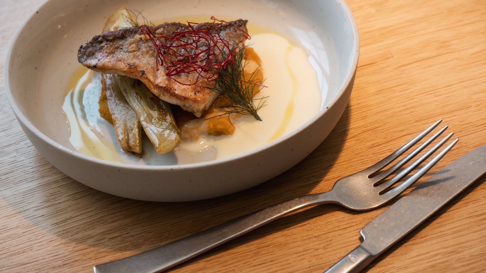 Gebratener Fisch mit Gemüse und Sauce in einer weißen Schale auf Holztisch