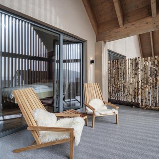 Hotel mit frühem Check-in Balkon mit zwei Holzstühlen mit Fellbezügen und Glas-Schiebetür vor Schlafzimmer