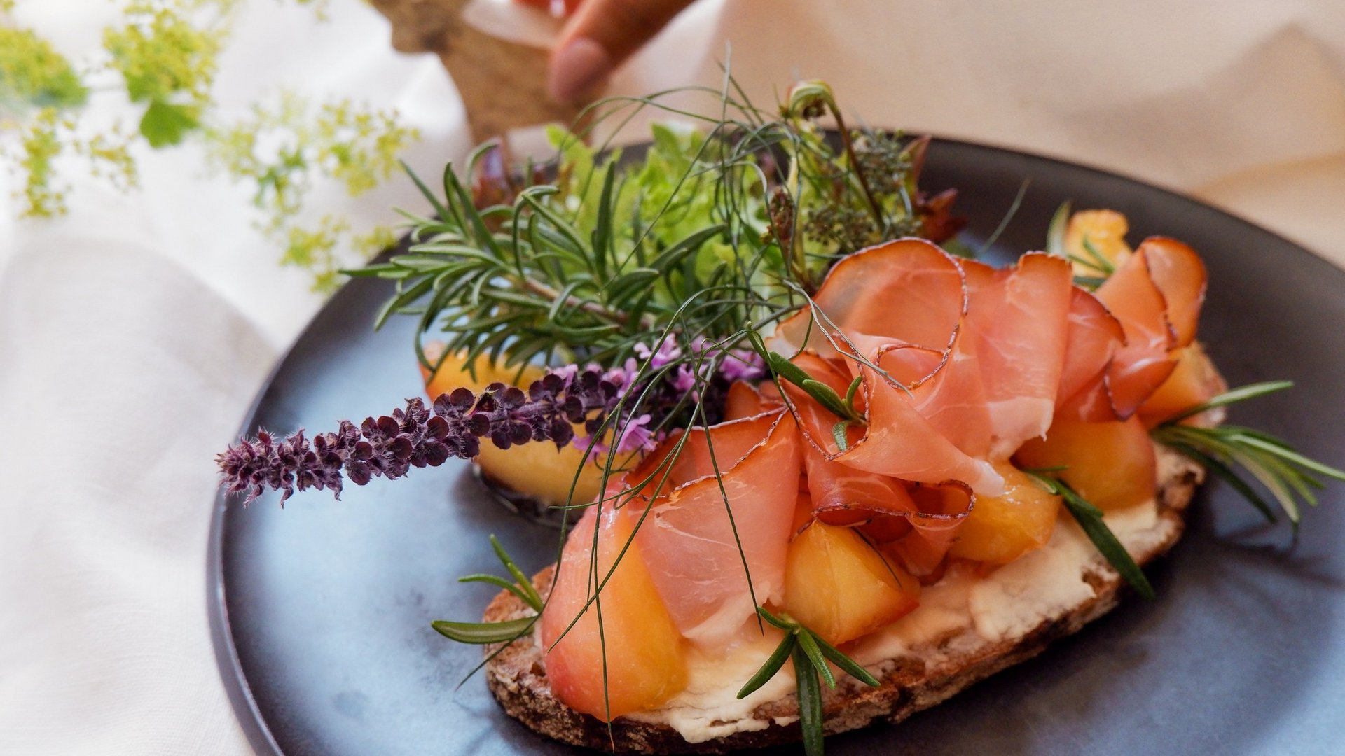 Home Open sandwich with ham, melon, and fresh herbs on a black plate