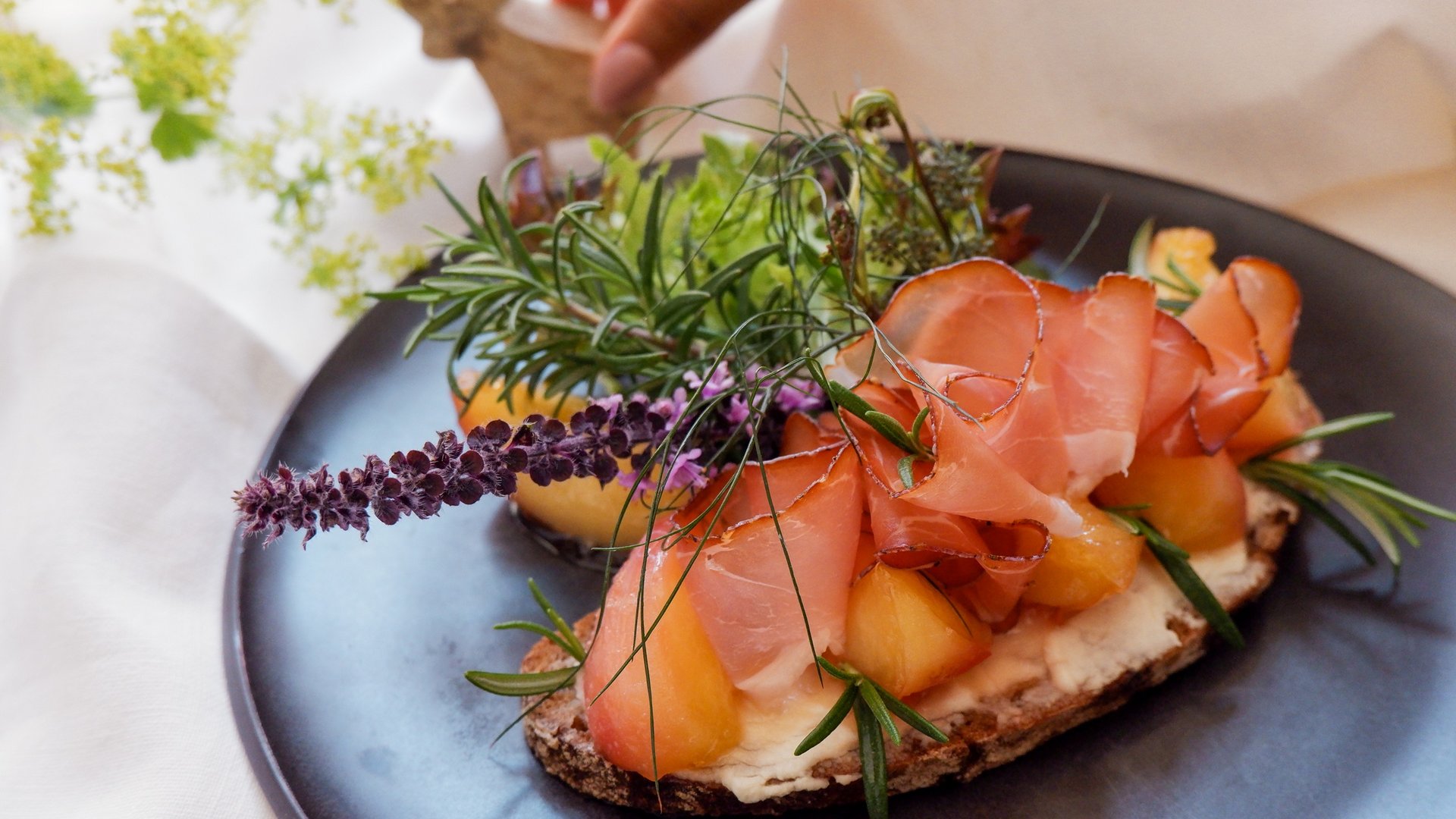 Romantik Hotel Hirschen: cuisine Open sandwich with ham, melon, and fresh herbs on a black plate