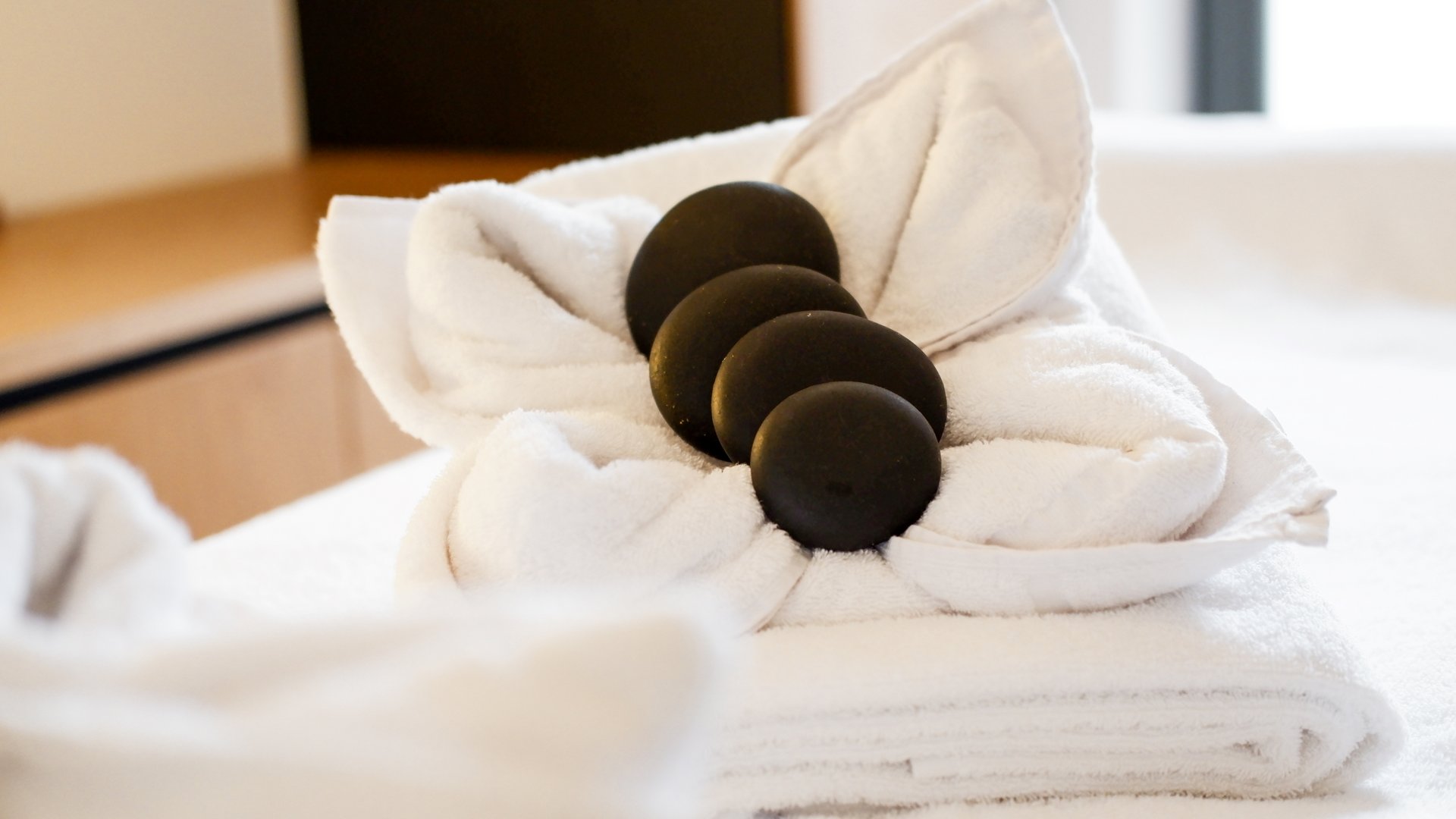 Revel in anticipation White towels folded with black massage stones on top