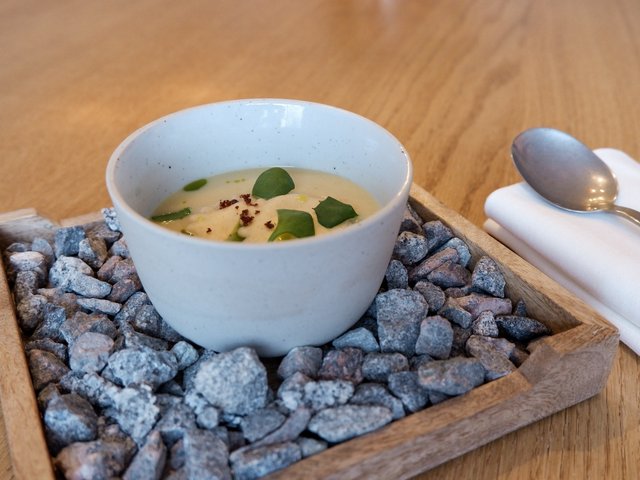 Romantik Hotel Hirschen: Bildergalerie Kleine Schüssel mit cremiger Suppe auf Holztablett mit Steinen daneben Löffel und Serviette